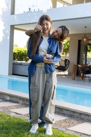 Two women celebrating new home by poolside holding key fob and embracing