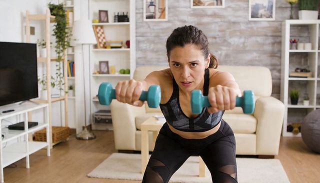 Woman training with teal dumbbells in modern living room for home strength workout
