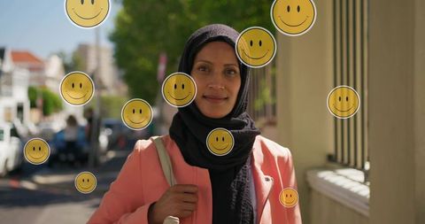 Confident muslim woman in hijab coral blazer with yellow smile icons on sunlit city street