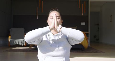 Asian Woman Meditates on Wooden Floor with Smartwatch in Bright Bedroom