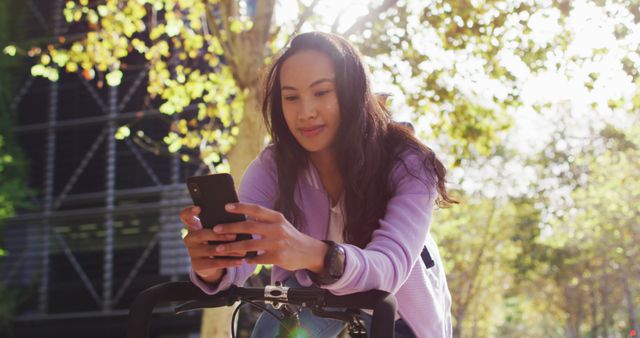 Asian woman with bicycle smiling while using smartphone in the park. modern lifestyle and living concept