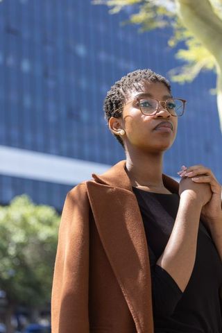 African american professional wearing brown coat and glasses by glass office tower