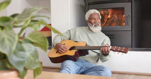 Senior Man Playing Guitar near Cozy Fireplace Warm Home Atmosphere