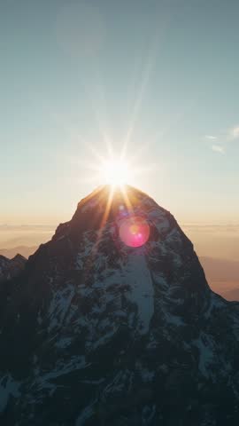 Sun rising over jagged alpine peak creating starburst and pink lens flare (vertical video)