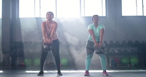 Sunlit Kettlebell Swings by Diverse Female Training Partners in Industrial Gym Studio