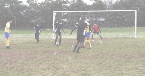 Player dribbling toward goal on muddy grass pitch during overcast amateur soccer match