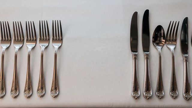 Polished silverware on white tablecloth showing symmetrical forks and knives for tabletop