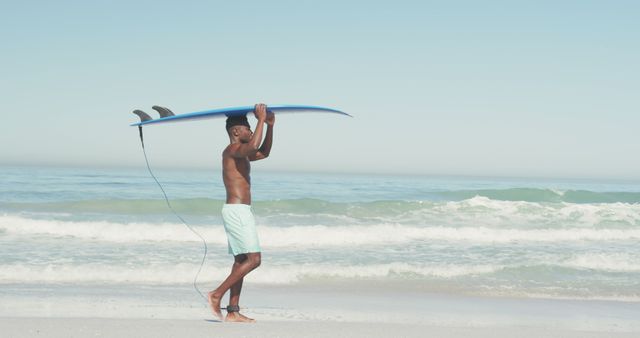 Young man walking along beach carrying surfboard on head during a sunny day. Perfect for advertisements and marketing materials related to summer activities, beach vacations, surfing, and coastal lifestyles. Ideal for promoting fitness, health, and outdoor leisure.