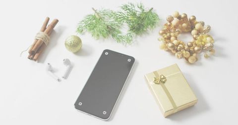 Minimalist festive flatlay featuring smartphone, gold gift box, pine sprig, wreath, cinnamon