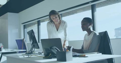 Female Colleagues Collaborating over Laptop in Bright Modern Office with City View