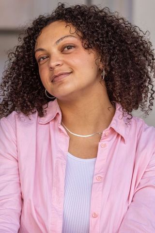 African american woman smiling and posing in pink shirt, wearing silver necklace