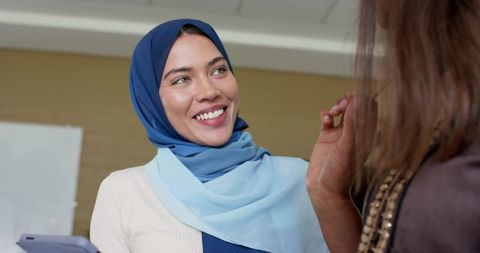 Indian professional woman wearing blue hijab smiling and conversing with colleague