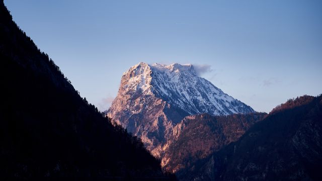 Stunning snow-capped mountain peak illuminated by sunrise, rising above a silhouetted valley. Ideal for use in outdoor adventure advertisements, travel brochures, nature photography themes, or inspirational poster designs. Captures serene and rugged beauty perfect for conveying majesty and tranquility.