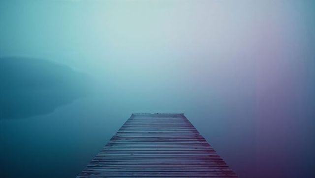 Weathered dock extends into foggy lake at dawn