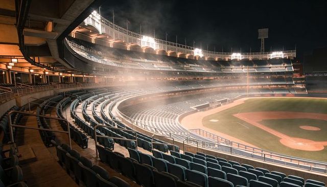 Empty nighttime baseball stadium showing curved teal seating bowl and lit infield
