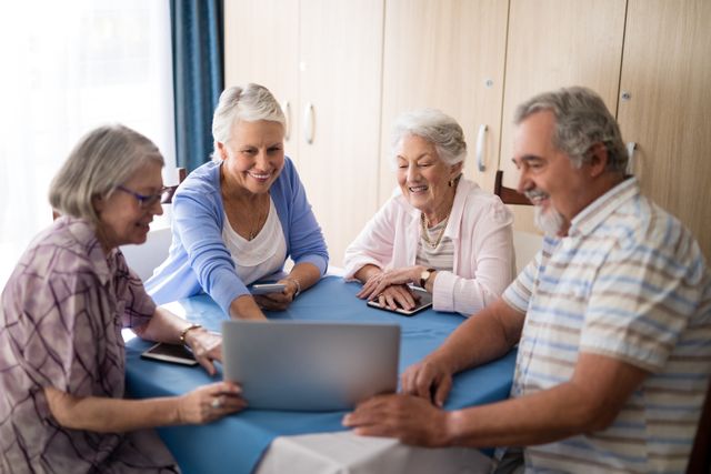 Group of seniors gathered around a laptop, smiling and engaging with technology. Ideal for illustrating senior living, digital literacy programs, community activities in retirement homes, and promoting social interaction among elderly individuals.