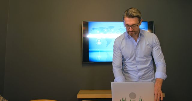 Businessman preparing for a presentation in a modern office with a laptop and screen in the background. Ideal for corporate, business, and technology-related uses like articles, websites, or brochures highlighting professional environments and working scenarios.