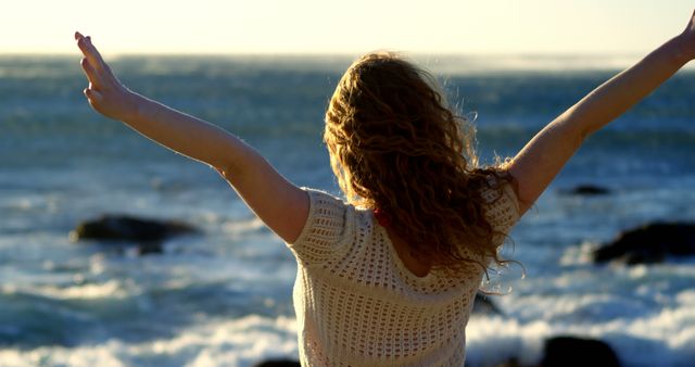 Woman with curly hair enjoying ocean breeze with arms outstretched - Download Free Stock Images Pikwizard.com