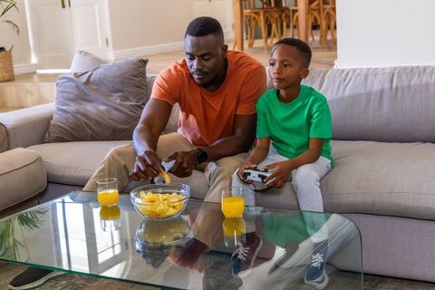 African American Father and Son Bonding While Playing Video Games and Sharing Snacks