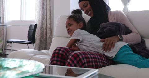 Smiling Mother Wearing Hijab Playing with Daughter on Sofa