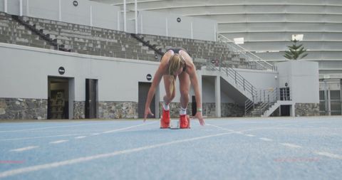 Female track athlete preparing in starting blocks on blue sprint track