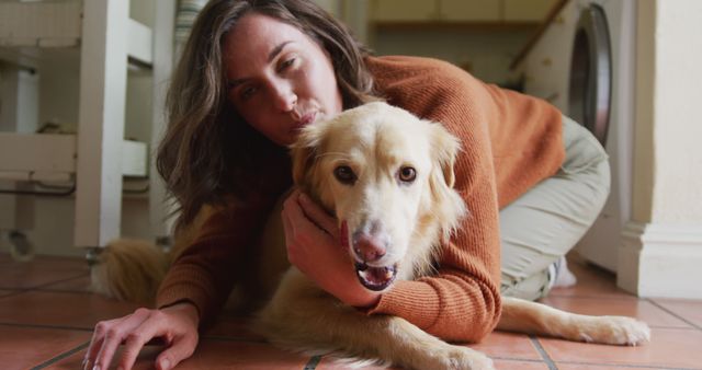 A woman is lying on a tiled floor in the kitchen, hugging her dog closely. The dog looks relaxed and content. This is a heartwarming moment showcasing the bond between a pet and its owner, making it perfect for themes related to pet care, family life, emotional wellbeing, and home comfort.