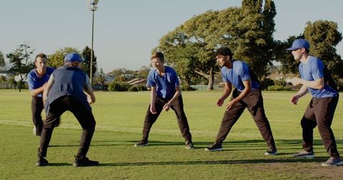 Five teammates practicing defensive stance on sunlit community sports field during training