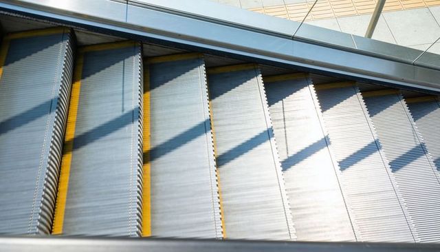 Sunlight Catching Ribbed Escalator Treads with Yellow Safety Strips Forming Diagonal Shadows