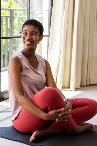 African american woman practicing yoga at home on mat smiling by sunny balcony window