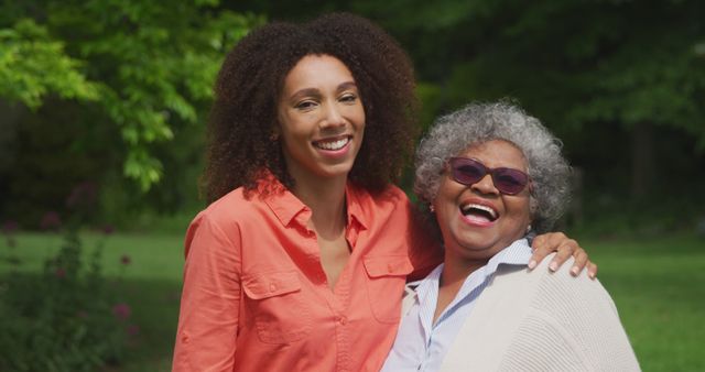 Portrait of happy african american grandmother with adult daughter embracing in sunny garden. Nature, domestic life and lifestyle, unaltered.