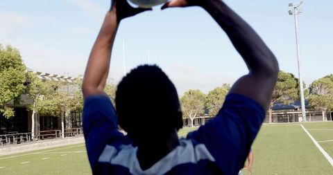 Soccer Player Raising Ball for Throw-In on Sunlit Field Showing Athletic Focus and Teamwork
