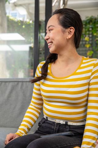 Smiling Asian Woman Relaxing Indoors with Smartphone on Sofa