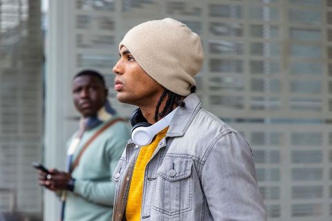Urban commuter wearing beanie and headphones, looking thoughtful at city transit stop