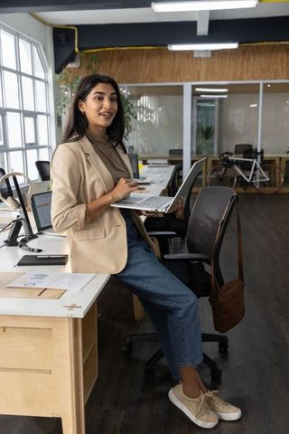 Indian woman entrepreneur reviewing charts while working on laptop in modern coworking office