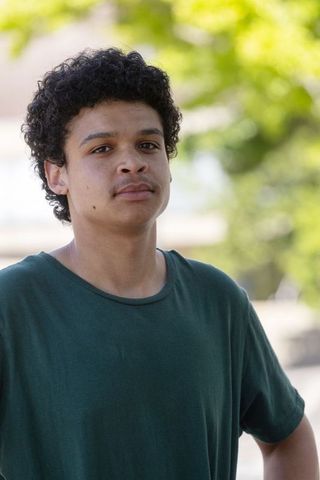 African young man standing outdoors wearing green t-shirt sunlit bokeh portrait