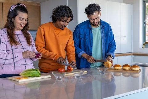 Diverse friends preparing burger ingredients on glossy kitchen island in bright daylight