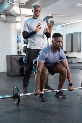 Trainer coaching male athlete performing loaded barbell squat for strength and technique