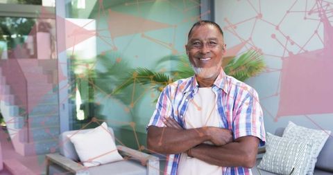 Smiling senior man standing with crossed arms on modern patio with tropical greenery