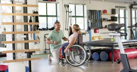 Physical therapist providing wheelchair rehabilitation and mobility training in modern gym