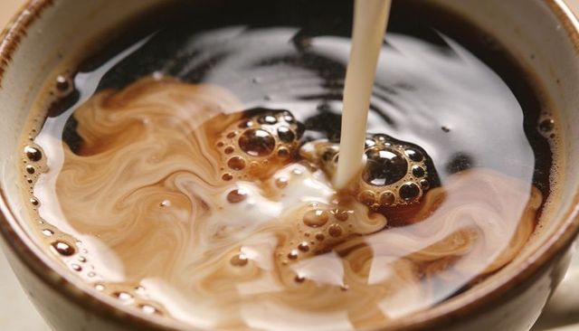 Pouring cream into coffee creating swirling latte art and smooth marble milk patterns