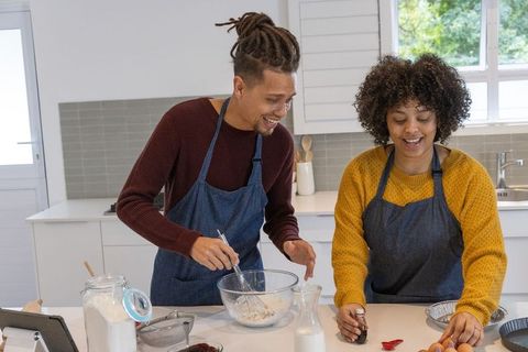 African american couple baking together in modern sunlit kitchen, smiling and mixing batter