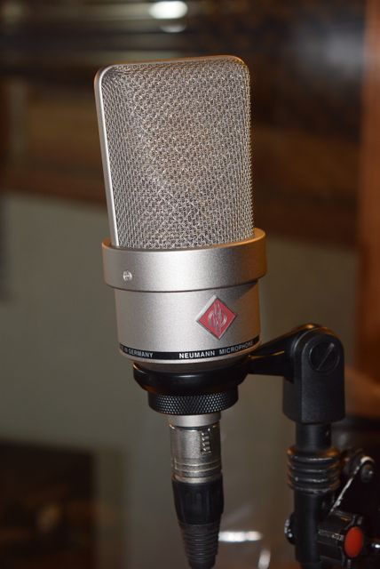 Close-up view of a silver professional condenser microphone mounted on a stand, suitable for use in a recording studio. Perfect for illustrating concepts related to music production, studio recording, podcasting, broadcasting, or sound engineering. Ideal for blogs, articles, or advertisements focusing on audio technology and professional recording equipment.
