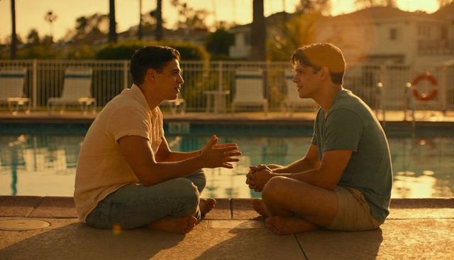 Two men having intimate conversation on pool deck during golden hour sunlight and warmth