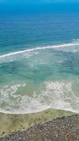 Drone rising over rocky shore with turquoise waves breaking and reef revealing sand