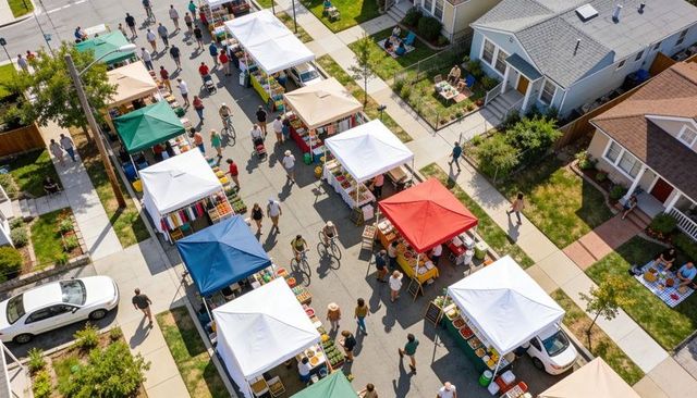 Aerial view neighborhood farmers market with colorful tents, crowds strolling, vendors selling