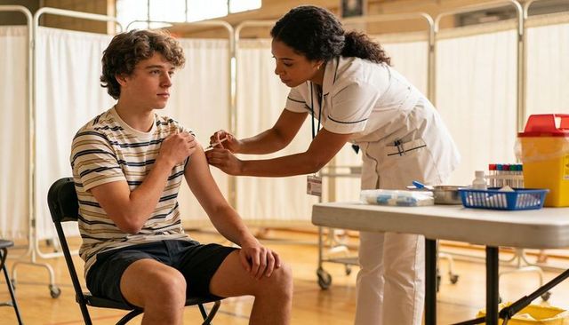 Teenager receiving vaccination in school gym clinic while nurse administers injection