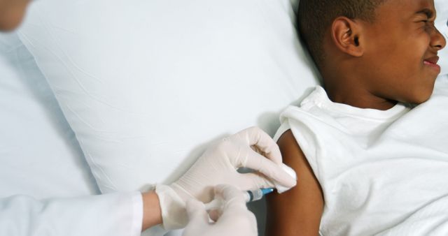 Young boy getting vaccinated by a medical professional wearing gloves. The boy is slightly pained. Suitable for content related to healthcare, pediatric medicine, vaccination campaigns, and virus prevention in children.