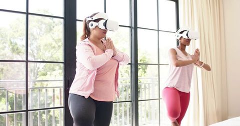 Women Practicing VR Yoga in Sunlit Living Room for At-Home Virtual Fitness