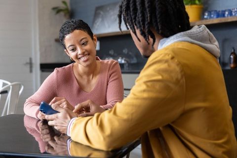 African american friends smiling and sharing smartphone at kitchen counter, casual lifestyle