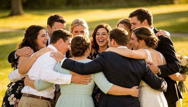 Wedding party embracing on sunlit lawn laughing and celebrating love and friendship